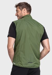 Grüne, leichte Weste mit glatter Textur, ärmellosem Design und einem subtilen reflektierenden Detail am Saum, kombiniert mit einem schwarzen T-Shirt.