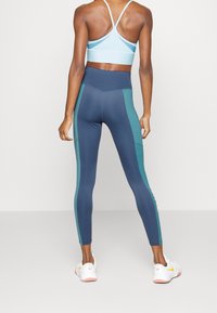 Legginsy sportowe w ciemnoniebieskim kolorze z turkusowymi panelami bocznymi, wysokim stanem oraz jasnoniebieskim stanikiem sportowym z tyłem w kształcie wyścigu.