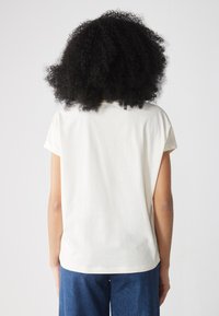 Krämfärgad t-shirt med kort ärm och avslappnad passform. Mjukt tyg och rundad fåll. Bärs tillsammans med blå vida jeans.