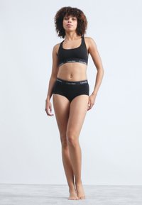 Μαύρο αθλητικό σουτιέν από βαμβάκι και ασορτί σλιπ με λογότυπο στη ζώνη, με εφαρμοστή σχεδίαση και λεία υφή. Χωρίς ορατά σχέδια ή διακοσμητικά.