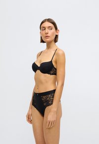 Černá krajková podprsenka s tvarovanými košíčky a nastavitelné ramínka, doplněná o černé kalhotky s vysokým pasem a květinovými krajkovými detaily po stranách.