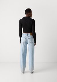 Svart ribbet langermet polo-skjorte kombinert med høyhalsede lyseblå denimjeans, med en rett passform og subtile detaljer på baklommene.