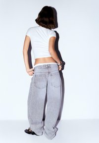 Helles graue weit geschnittene Jeans mit hoher Taille, ausgestattet mit Gesäßtaschen und einer ausgewaschenen Textur, kombiniert mit einem figurbetonten weißen T-Shirt und schwarzen Schuhen.