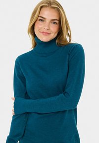 Maglione a collo alto teal con maniche lunghe, texture morbida e design aderente. Presenta un colletto e polsini a coste, senza motivi o accenti visibili.