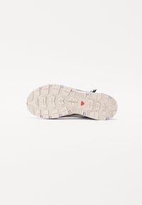 Leichter Sportschuh mit einem strukturierten grauen Obermaterial und einer cremefarbenen Gummisohle, die tiefe Profilierungen und lilafarbene Akzente aufweist.