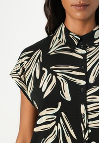 Czarna koszula z krótkim rękawem, zdobiona jasnobeżowymi i niebieskimi wzorami liści. Posiada kołnierz oraz czarne guziki na froncie.