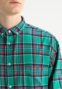 Camicia button-up a quadri verdi con linee contrastanti rosa, bianche e navy. Il tessuto appare morbido con un design di colletto classico.