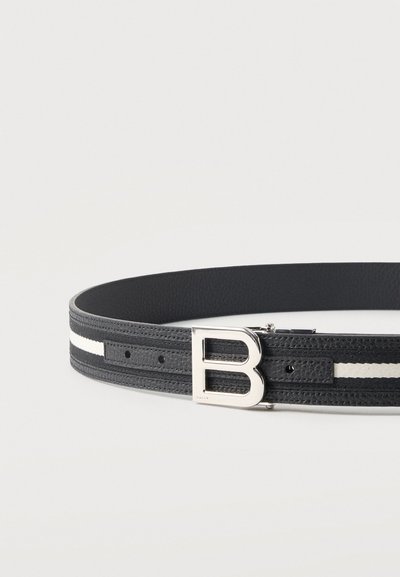 Μαύρη δερμάτινη ζώνη με λευκή λωρίδα και ασημένια πόρπη σε σχήμα του γράμματος «B» τοποθετημένη επίπεδη σε φωτεινή επιφάνεια.