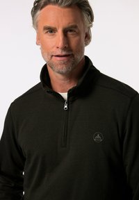 Svart halvdraget tröja i texturerad tyg med subtila ränder och broderad logotyp på vänster bröst. Dragkedja vid halsringningen.