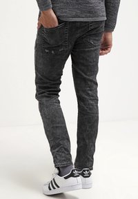 Jeans en denim noir avec une finition délavée, coupe slim, poches arrière et une paire de baskets blanches contrastantes avec des accents noirs.