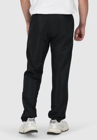 Schwarze, leichte Sporthose mit elastischem Bund, schmal zulaufenden Beinen und gerippten Knöcheln, kombiniert mit silbernen und weißen Turnschuhen.