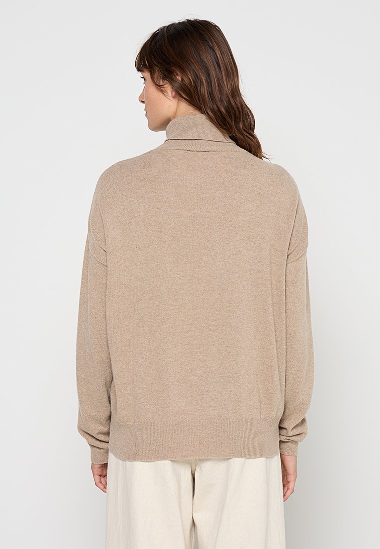 Maglione lavorato a maglia beige con colletto alto, taglio comodo e polsini a coste. Texture morbida, design minimalista e dettagli sul retro senza cuciture.
