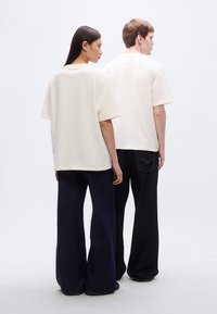 Ενιαία oversized κρεμ T-shirts συνδυασμένα με τζιν σκούρου χρώματος με φαρδιές παντελόνες. Το ύφασμα φαίνεται απαλό, με άνετη εφαρμογή και ελάχιστες λεπτομέρειες.