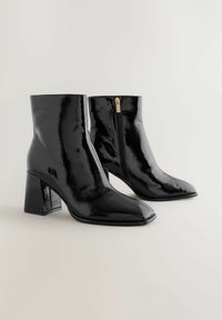 Czarne, lakierowane botki za kostkę z kwadratowym noskiem, masywnym obcasem i bocznym zamkiem błyskawicznym z złotym uchwytem. Gładka, błyszcząca tekstura.