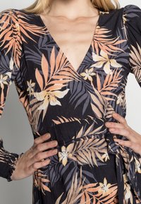 Vestido negro ajustado con estampado floral tropical que presenta hojas naranjas y amarillas. Las largas mangas abullonadas y la cintura atada acentúan su diseño.