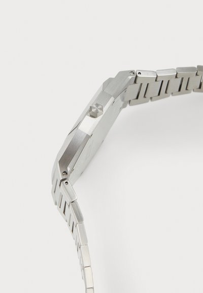 Silberner Edelstahl-Uhr mit einem achteckigen Gehäuse, strukturierten Oberflächen, hervorstehender Krone und einem armbandähnlichen Design mit segmentierten Gliedern.