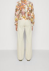 Giacca a fiori con maniche lunghe in tessuto multicolore, abbinata a pantaloni larghi color beige chiaro. Adatta per un look casual.