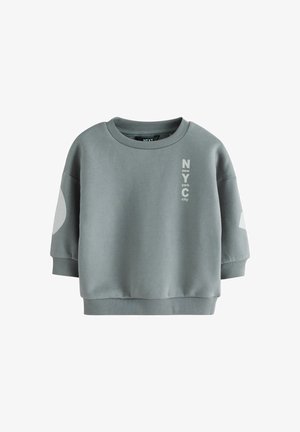 Grå cropped sweatshirt lavet af bomuldsblandet stof. Har en rund halsudskæring, oversized ærmer og trykt tekst "NYC" i kontrastfarve.