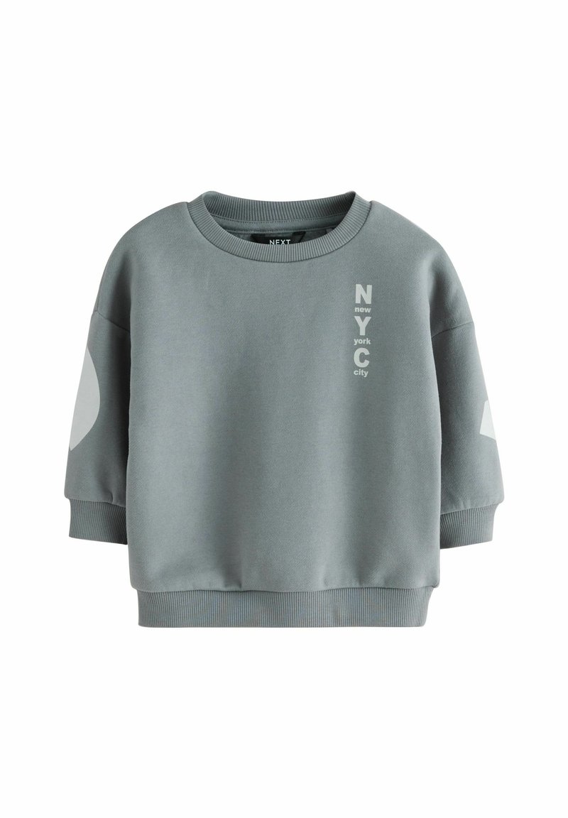 Bluza scurtă gri, confecționată dintr-un material din amestec de bumbac. Are un decolteu rotund, mâneci supradimensionate și un text imprimat "NYC" în culoare contrastantă.