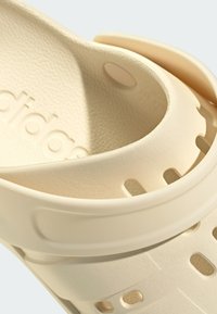 Sandale moulée beige clair avec une surface texturée, des trous latéraux pour la ventilation et un logo surélevé sur la sangle.