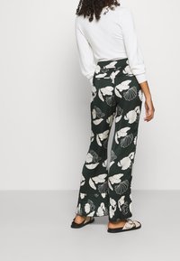 Zielone, luźne spodnie w kwiatowy wzór w białym kolorze. Elastyczny pas i szerokie nogawki. Połączone z czarnymi sandałami.