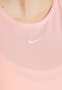 Acercamiento de una persona que lleva puesta una camiseta deportiva rosa claro con un pequeño logo blanco de Nike cerca del pecho.