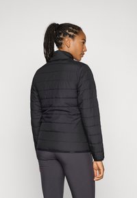 Giacca nera imbottita con cuciture orizzontali, collo alto e texture liscia. Design aderente. Si abbina a leggings scuri e sinuosi.