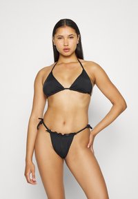 Biquíni preto com um top triangular e uma parte de baixo em tanga com babados, feito de um tecido suave com laços ajustáveis nas laterais.