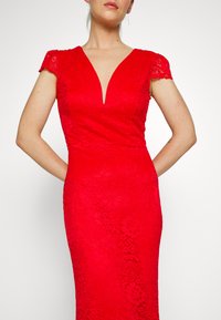 Vestido vermelho rendado com decote em V profundo e mangas curtas, apresentando padrões florais e uma silhueta ajustada. Textura suave em toda a peça.