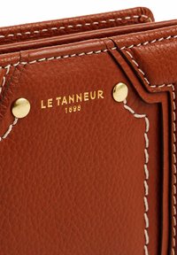 Portafoglio in pelle marrone con cuciture visibili e dettagli in oro. Presenta il testo impresso "LE TANNEUR 1898" sul fronte.