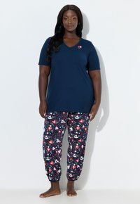 Laivastonsininen V-kaula-aukkoinen T-paita, jossa on lyhyet hihat, yhdistetty kuvioituihin pyjamahousuihin, joissa on punaisia, vaaleanpunaisia ja valkoisia sydämiä tummalla taustalla.