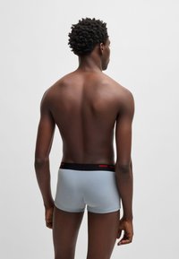 Light blue boxer shorts with a black waistband featuring red "HUGO" branding, viewed from the back against a plain background.