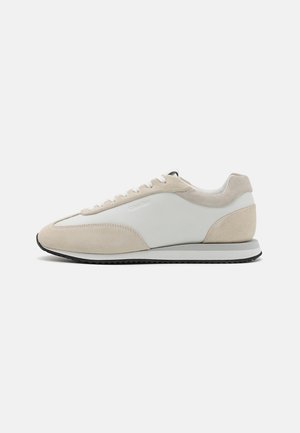 Beige semsket læder og hvidt læder sneakers med rund tå, flade snørebånd, polstret sål og sort gummisål.