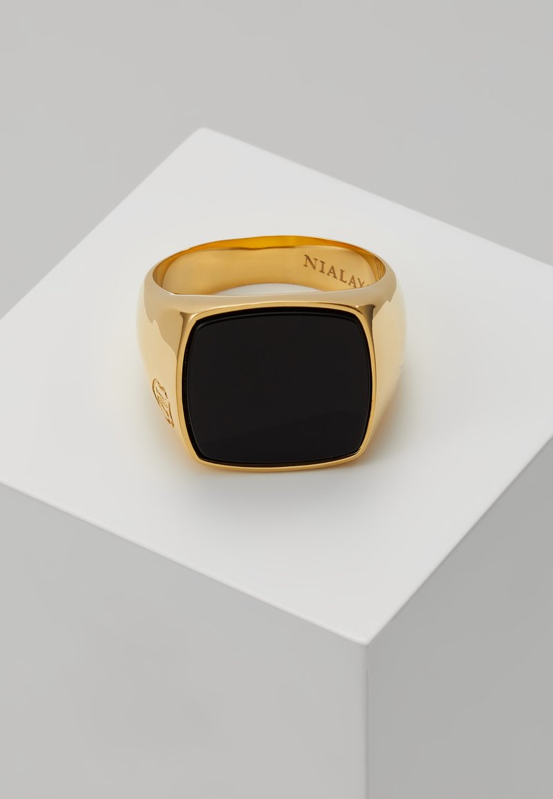 Guldfarvet ring med en firkantet sort stensætning, glat overflade og en let buet ring. Indgraveret mærkenavn indeni ringen.