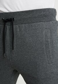 Pantaloni joggers grigi realizzati in tessuto morbido, con vita elasticizzata e cordino, tasche laterali e una texture liscia.