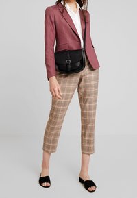 Bordo přiléhavý blazer, bílá košile, hnědé kostkované kalhoty, černá crossbody taška s přezkou a černé skládací sandály. Texturovaná látka a střih na míru.