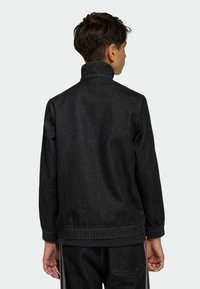 Svart jeansjacka med hög krage, elastisk fåll och muddar. Tyget har en texturerad yta och kompletteras av en minimalistisk design.