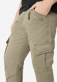 Beige cargo pants made of textured fabric featuring multiple pockets, a zippered pocket, and reinforced stitching along the seams.