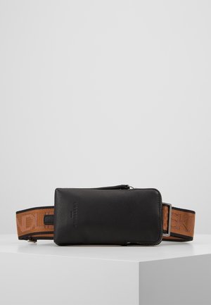 Sac banane en cuir noir avec une sangle marron réglable comportant un texte en relief, présenté sur une surface blanche sur fond gris.
