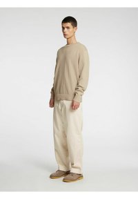 Beige langermet strikkegenser med rund hals, kombinert med vide kremfargede bukser og gråbrune sko med lys såle.