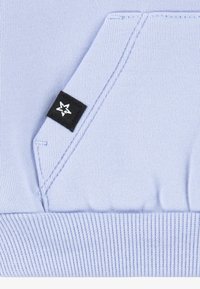 Hele sinine kapuutsiga dressipluus lähivõte, millel on kängurutasku, soonikserv ja must silt, millel on valge tähelogo tasku serval.