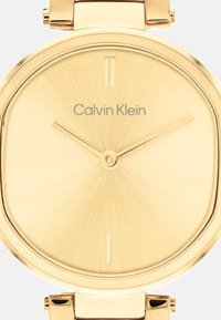 Złocony zegarek Calvin Klein o okrągłym, minimalistycznym designie. Teksturowana tarcza, smukłe wskaźniki godzinowe i gładki metalowy bransoletka.