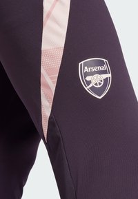 Leggings de sport violets avec un panneau latéral texturé rose et le logo d'Arsenal sur la cuisse droite. Fabriqués en tissu extensible et respirant.