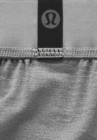 Graue Sportshorts aus strukturiertem Stoff mit einem gerafften Bündchen und schwarzem Logo-Detail. Sichtbare Nähte entlang der Kante.