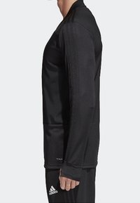 Sudadera atlética de manga larga negra, hecha de una tela suave, que cuenta con agujeros para los pulgares, un dobladillo redondeado y tres líneas a lo largo de cada costura del hombro.