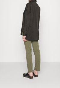 Oversized dark brown shirt with a collar, paired with olive green pants and black clogs featuring metal studs on a wooden sole.