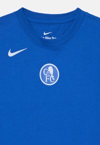Blå sports T-skjorte med hvit Nike-logo på høyre bryst og sirkulært Chelsea FC-emblem i midten.