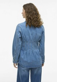 Cămașă din denim cu o siluetă ajustată, mâneci lungi și un design cu pliu la spate. Culoare albastru deschis cu cusături și detalii de butoni în contrast.