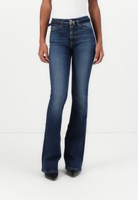 Uitlopende donkerblauwe denim jeans met een hoge taille, voorzien van een zilveren gesp en riemlussen. Soepele textuur, contrasterende stiksels.