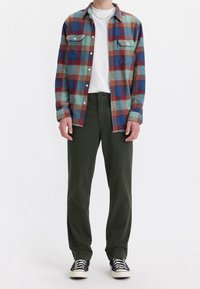 Flanellskjorta med ett flerfärgat rutmönster i blått, rött och turkos. Bärs över en vit t-shirt och kombineras med olivgrön byxor och svarta skor.